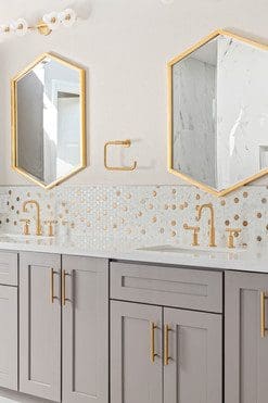 Stylish modern bathroom with gray vanity, gold accents, and elegant mosaic tile backsplash.