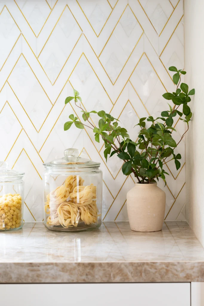 Modern kitchen corner with chevron backsplash, jars of pasta, and a vibrant green plant.