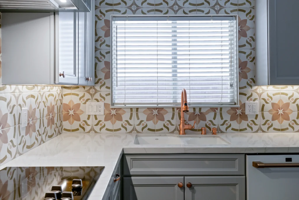 Chic kitchen with floral tile backsplash, gray cabinets, white countertop, and copper faucet accents.