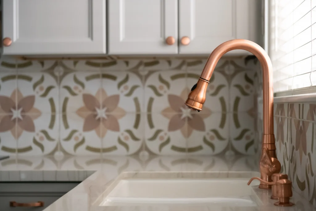 Elegant kitchen with a white sink, modern copper faucet, and vibrant floral backsplash.