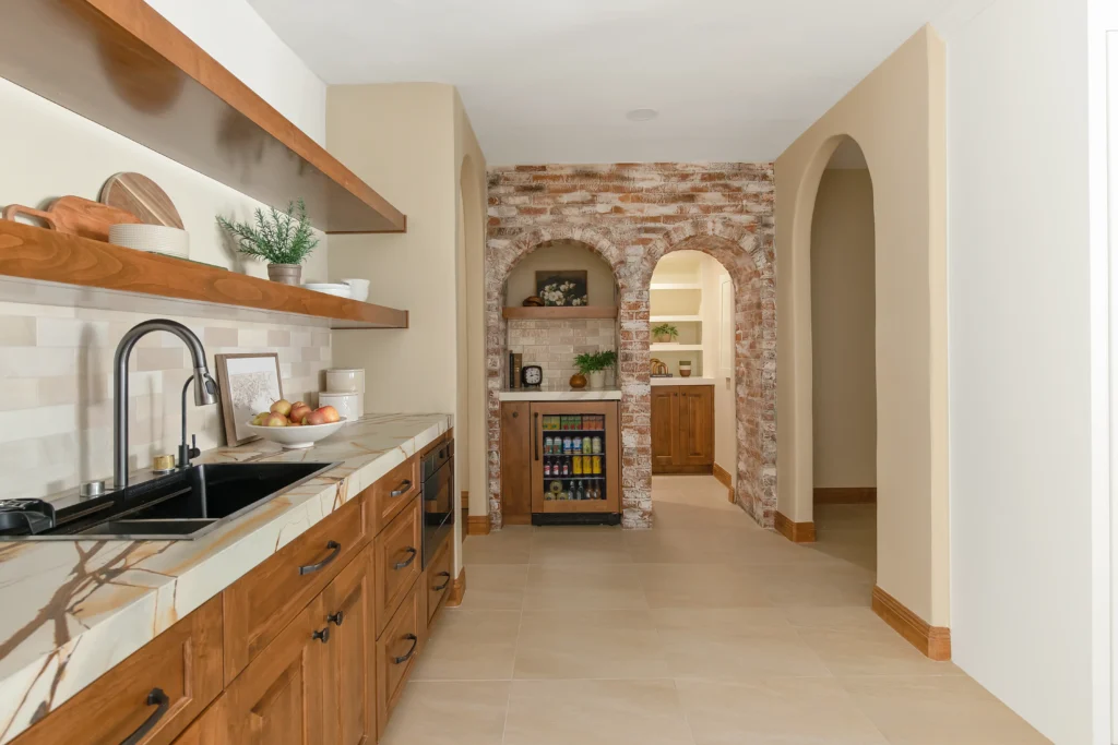 Stylish modern rustic kitchen with wood cabinetry, light countertops, and a charming stone archway.