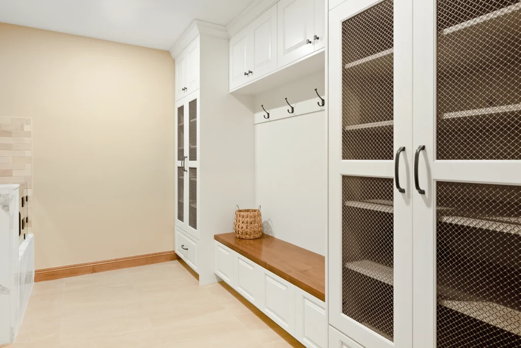 Stylish modern mudroom with white cabinetry, wooden bench, and functional hooks for organization.