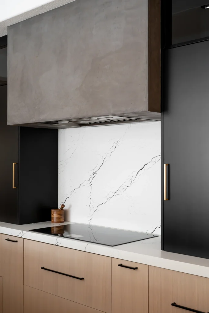 Modern kitchen with a sleek hood, elegant marble backsplash, and warm wood cabinetry.