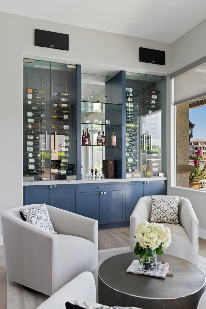 Elegant living corner with plush chairs, floral centerpiece, and stylish navy wine cabinet.