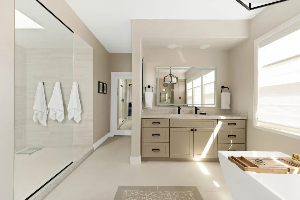 Elegant modern bathroom with warm hues, double vanity, glass shower, and abundant natural light.