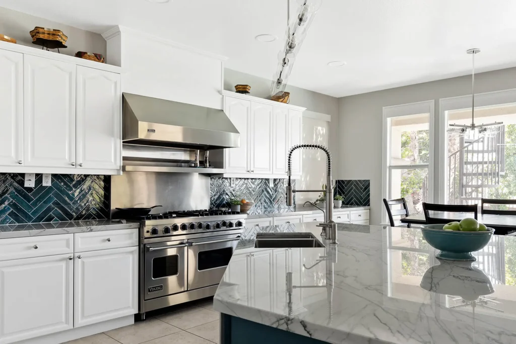 Sleek modern kitchen with teal herringbone backsplash, marble island, and stainless steel appliances.