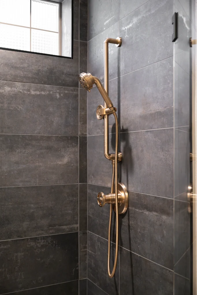 Luxurious modern shower in The Alps with elegant gold fixtures and serene gray tiles.