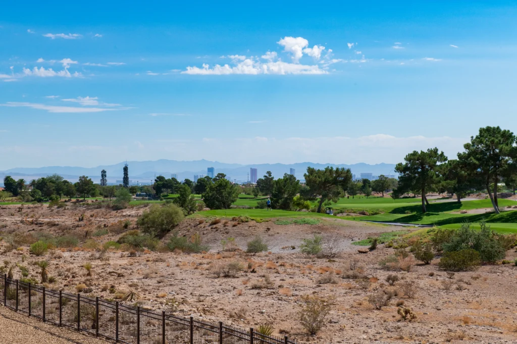 Arid terrain contrasts with urban greenery and skyline against distant mountains in sunny Indiana.