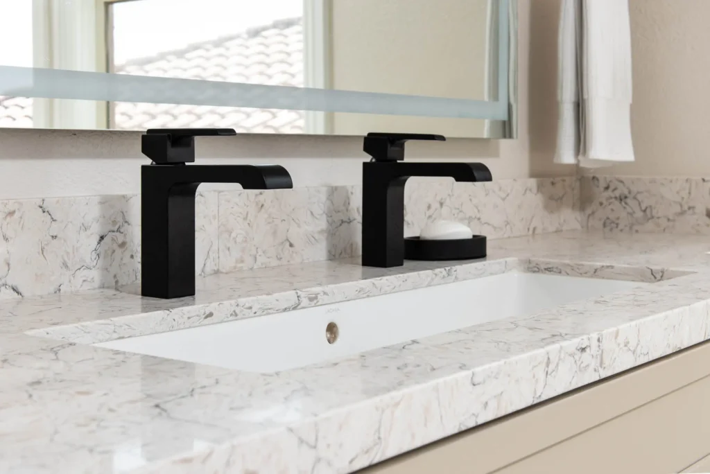 Elegant modern bathroom sink with white marble, black faucets, and minimalist accessories.