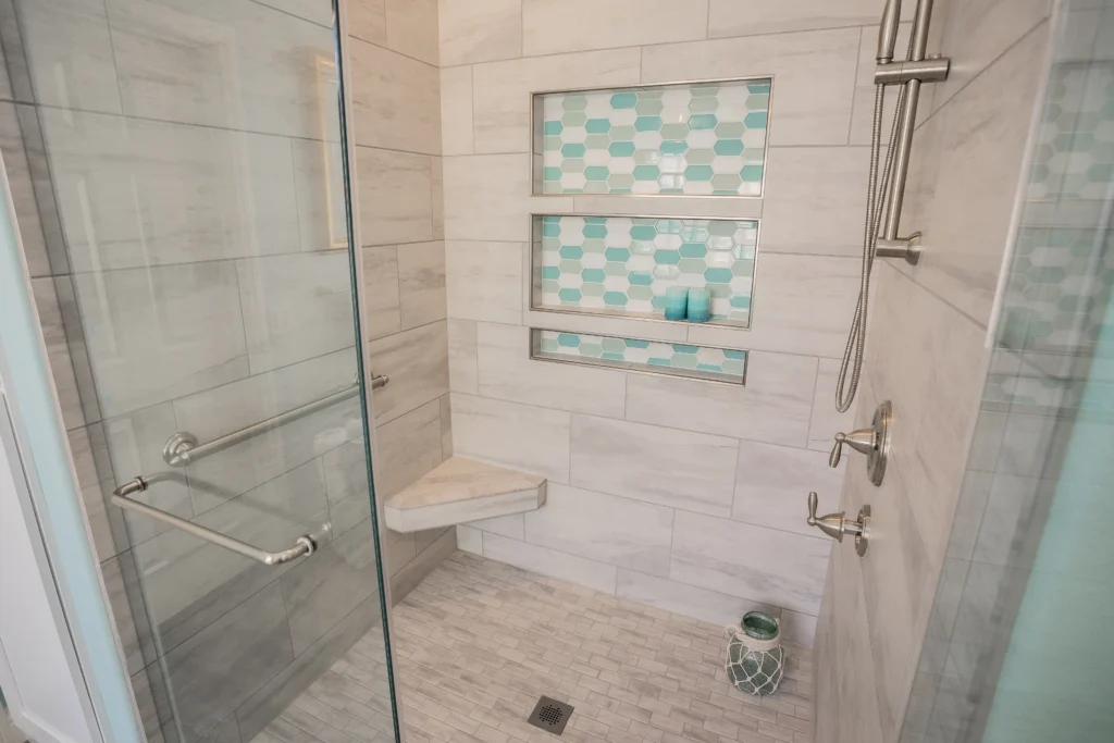 Chic shower design with glass enclosure, beige tiles, and aqua mosaic alcove for modern luxury.