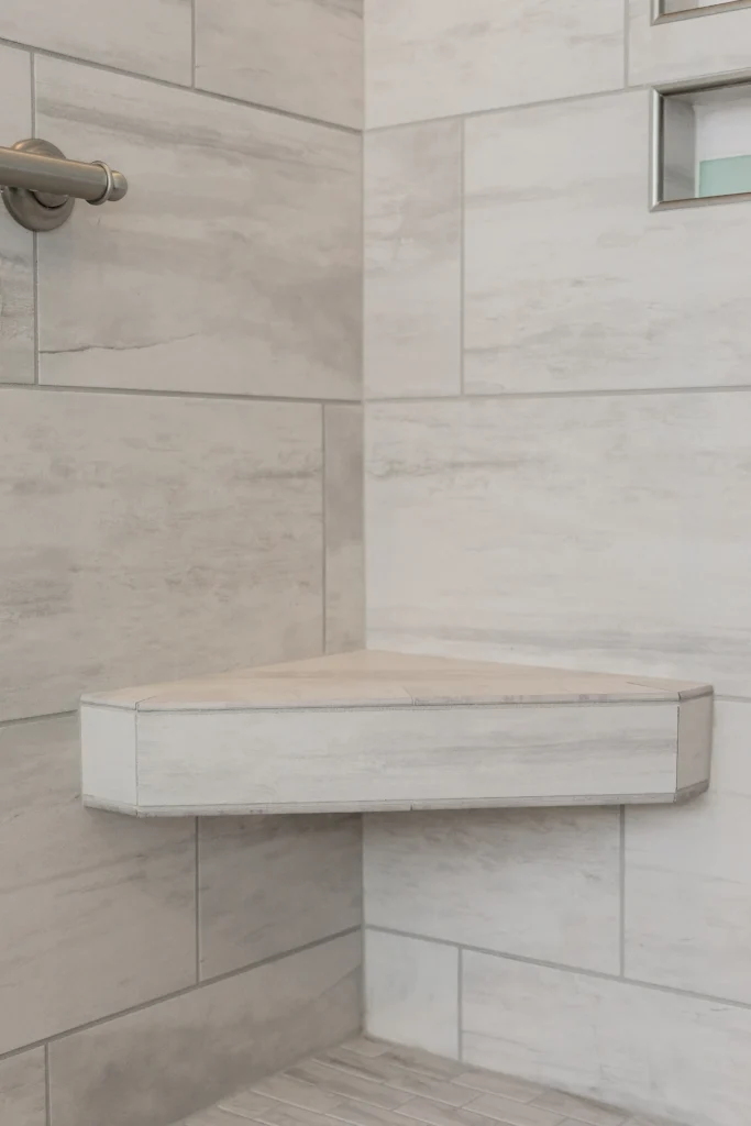 Minimalist shower corner with stone shelf, gray tiles, and stainless steel grab bar in sleek design.