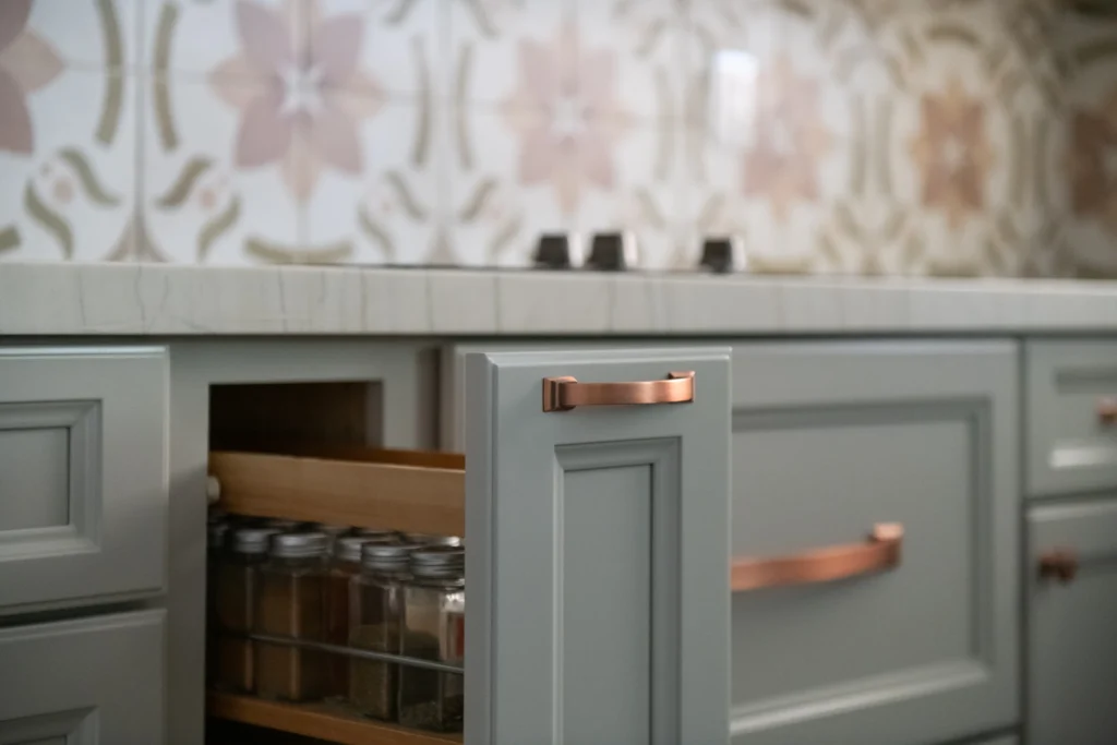 Modern kitchen with gray spice cabinet, copper handles, and floral tile backsplash for stylish organization.