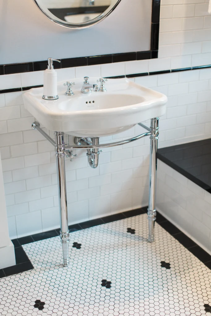 Modern bathroom design featuring a white pedestal sink, chrome accents, and black-and-white tiled flooring.