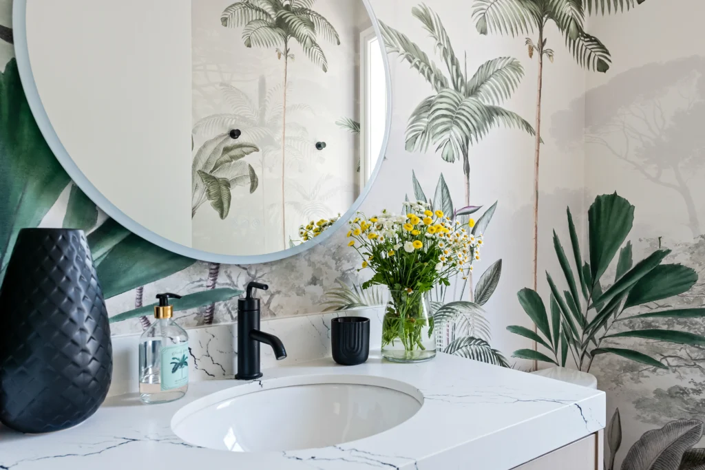 Modern bathroom featuring tropical wallpaper, white marble, and black fixtures for a luxurious retreat.