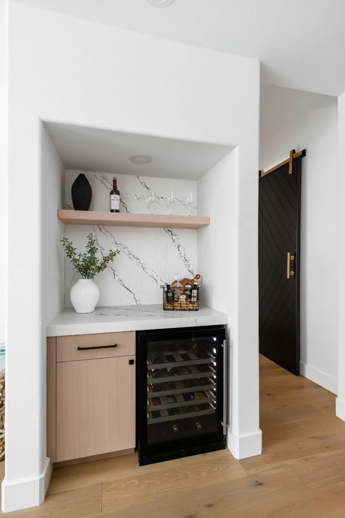 Chic mini-bar design with marble backsplash, light wood accents, and sleek black fridge.