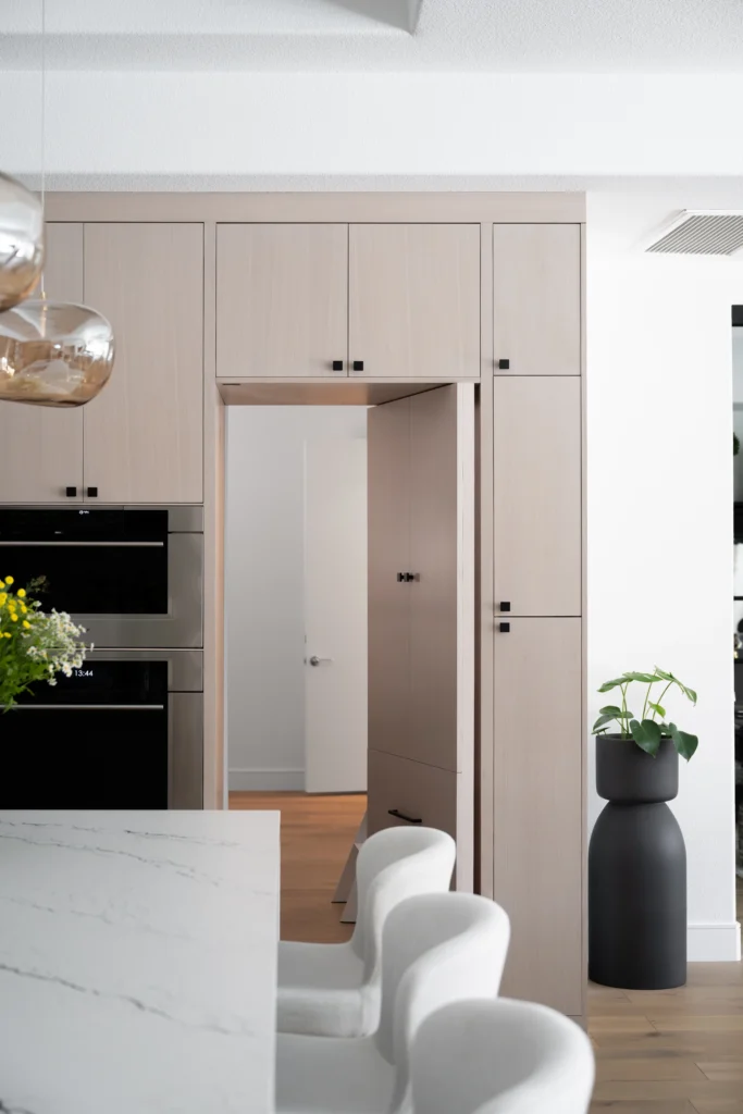 Sleek minimalist kitchen with beige cabinetry, black appliances, marble countertop, and stylish pendant lighting.