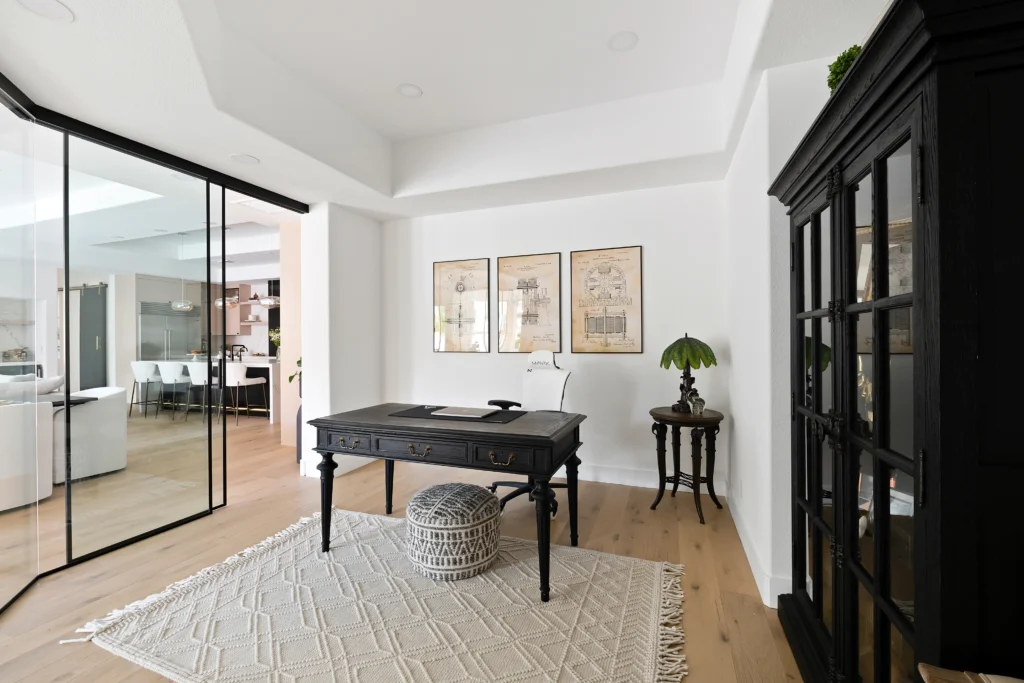 Modern minimalist home office with black desk, natural light, and artistic decor.