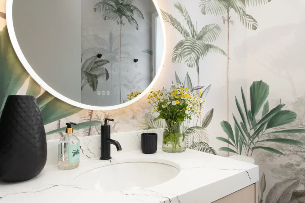 Serene modern bathroom with lighted mirror, botanical wallpaper, and stylish decor by Reveal Interior Design.