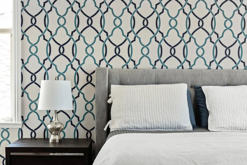 Modern bedroom with navy and aqua wallpaper, gray upholstered bed, and elegant natural lighting.