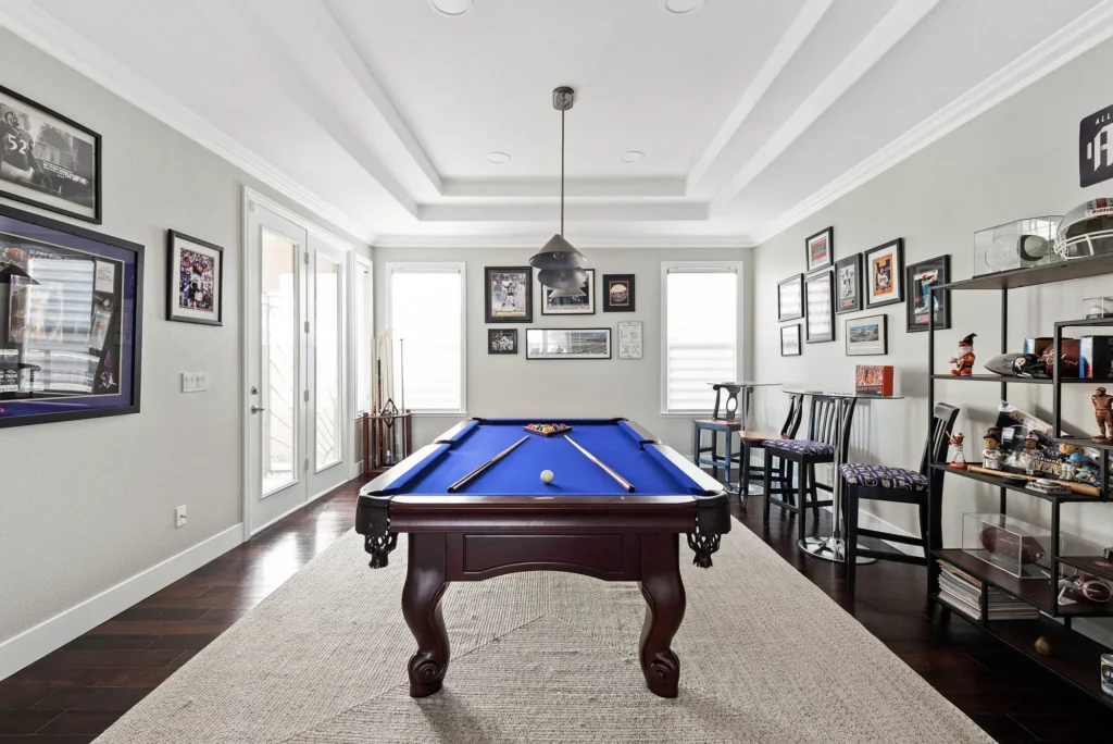 Sophisticated billiard room with blue felt table, curated art, and elegant bar seating.