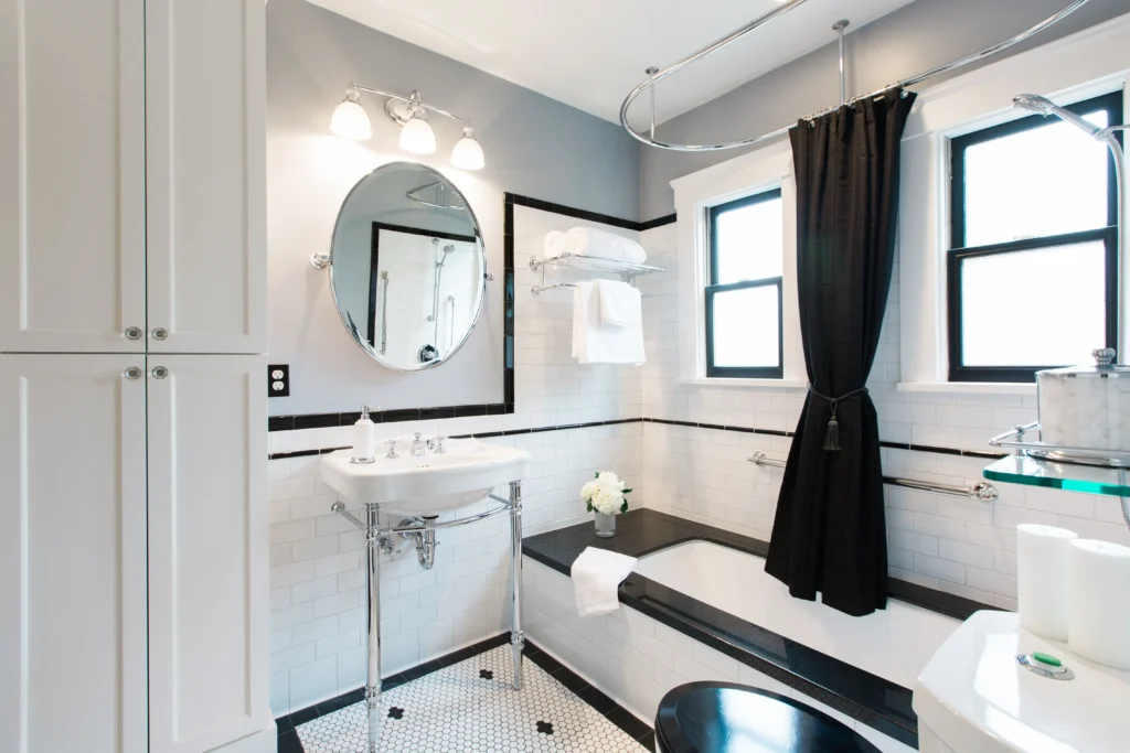 Modern bathroom with gray walls, white cabinetry, circular mirror, and natural light flooding through windows.