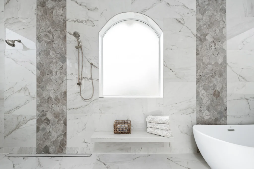 Sleek, elegant bathroom design with marble walls, natural light, and luxurious freestanding bathtub.