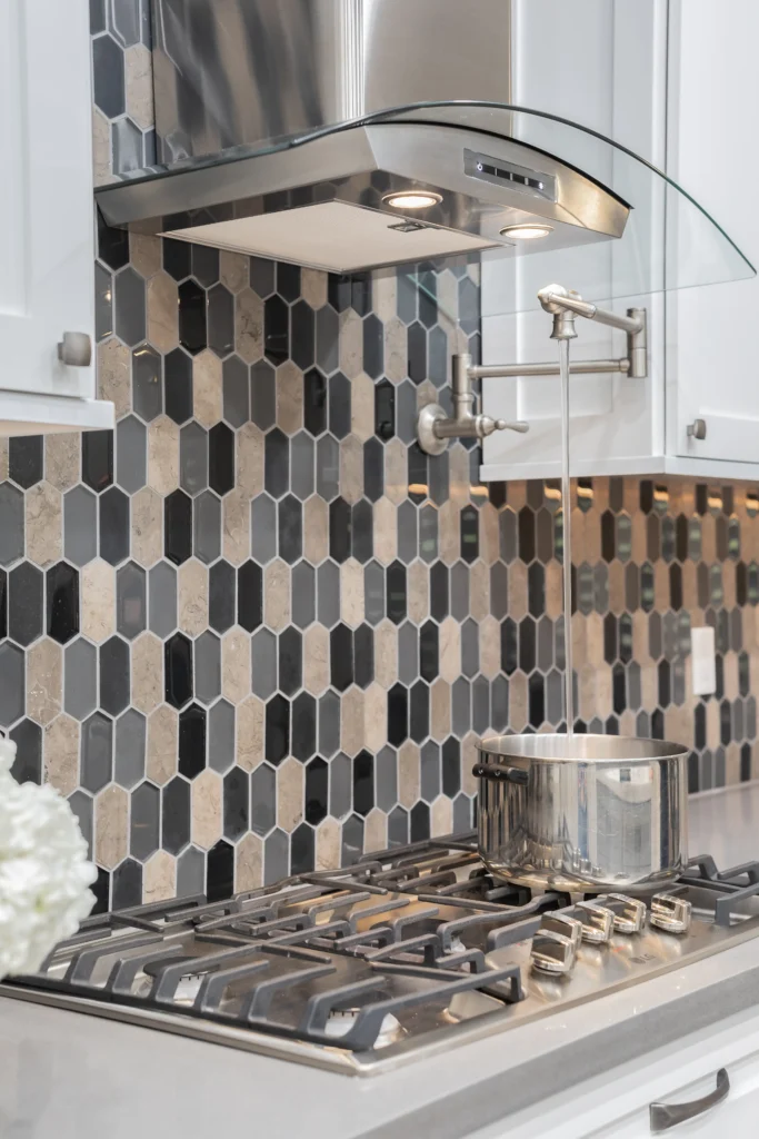 Contemporary kitchen featuring hexagonal backsplash, stainless steel stovetop, and fresh floral accents.