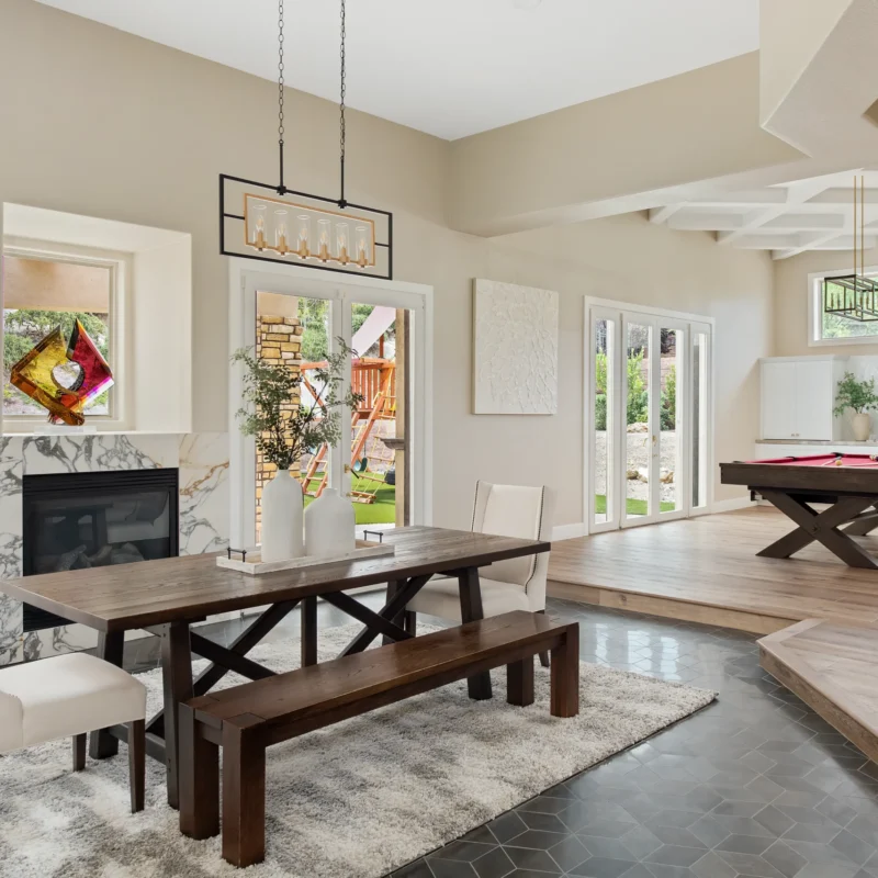 Chic open-concept living and dining area with dark wood table, billiards, and natural light.