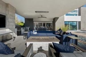 Chic outdoor living area with blue sectional sofa, fire pit, and modern kitchen amenities.