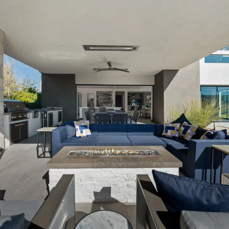 Chic outdoor living area with blue sectional sofa, fire pit, and modern kitchen amenities.