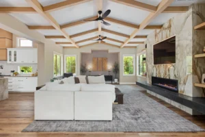 Modern living room with sectional sofa, stone wall, vaulted ceiling, and large windows.