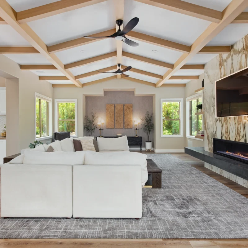 Modern living room with sectional sofa, stone wall, vaulted ceiling, and large windows.