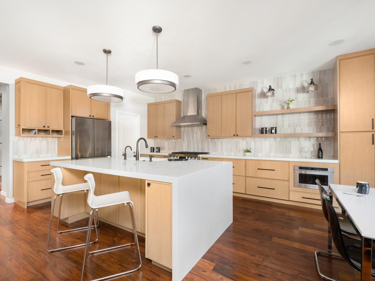Open-concept kitchen with warm oak cabinetry, quartz island, and handmade-style picket tile backsplash, Reveal Interior Design Las Vegas
