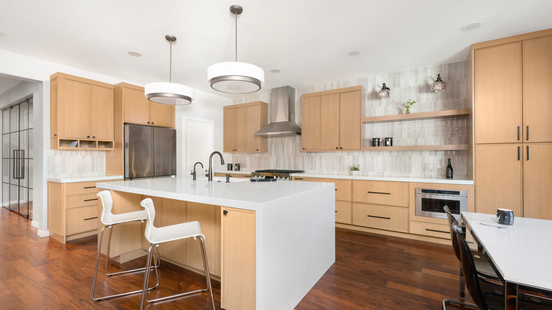 Open-concept kitchen with warm oak cabinetry, quartz island, and handmade-style picket tile backsplash, Reveal Interior Design Las Vegas