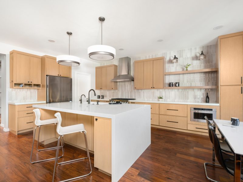 Open-concept kitchen with warm oak cabinetry, quartz island, and handmade-style picket tile backsplash, Reveal Interior Design Las Vegas