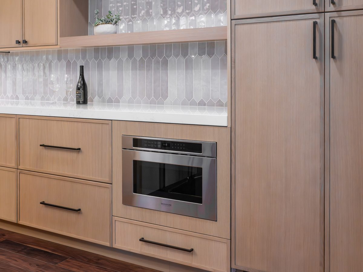 Kitchen with warm stained oak slim shaker cabinetry, dark bronze hardware, and picket-shaped backsplash tile, Reveal Interior Design Las Vegas