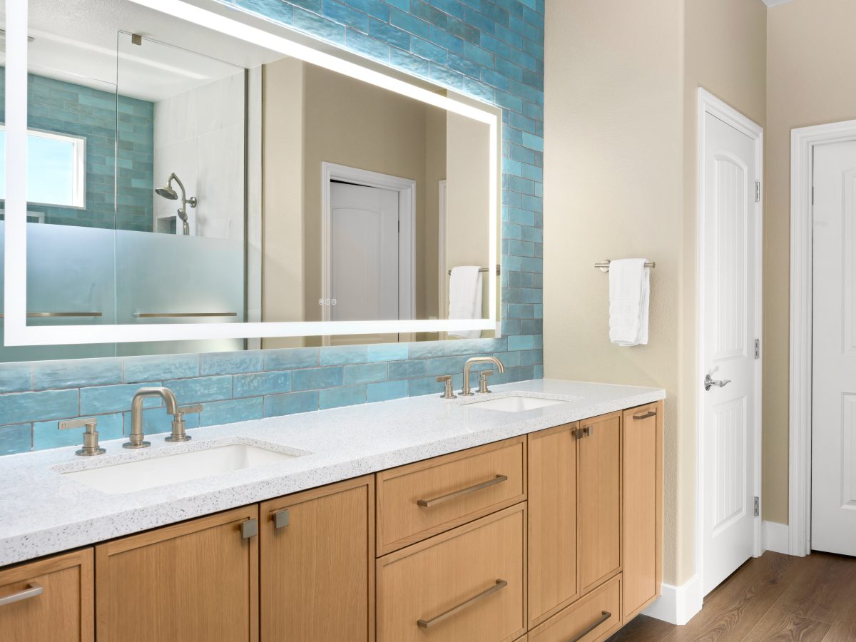 Primary bathroom double vanity with white quartz countertops, warm oak cabinetry, and handmade teal subway tile, Reveal Interior Design Las Vegas