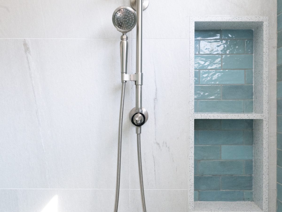 Primary bathroom shower with brushed nickel rain head, handshower, and teal handmade subway tile shampoo niches, Reveal Interior Design Las Vegas