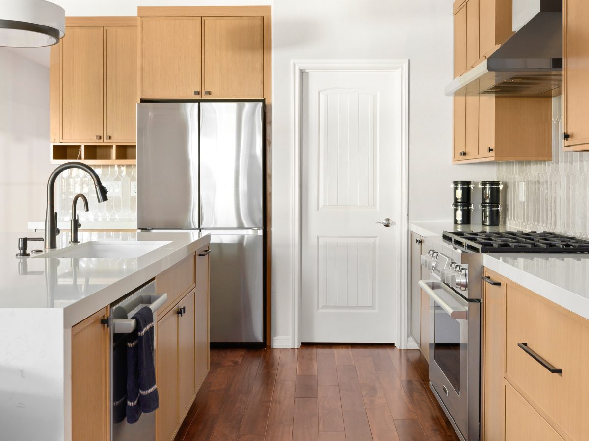 Galley kitchen with warm oak shaker cabinetry, quartz countertops, and stainless appliances, Reveal Interior Design Las Vegas