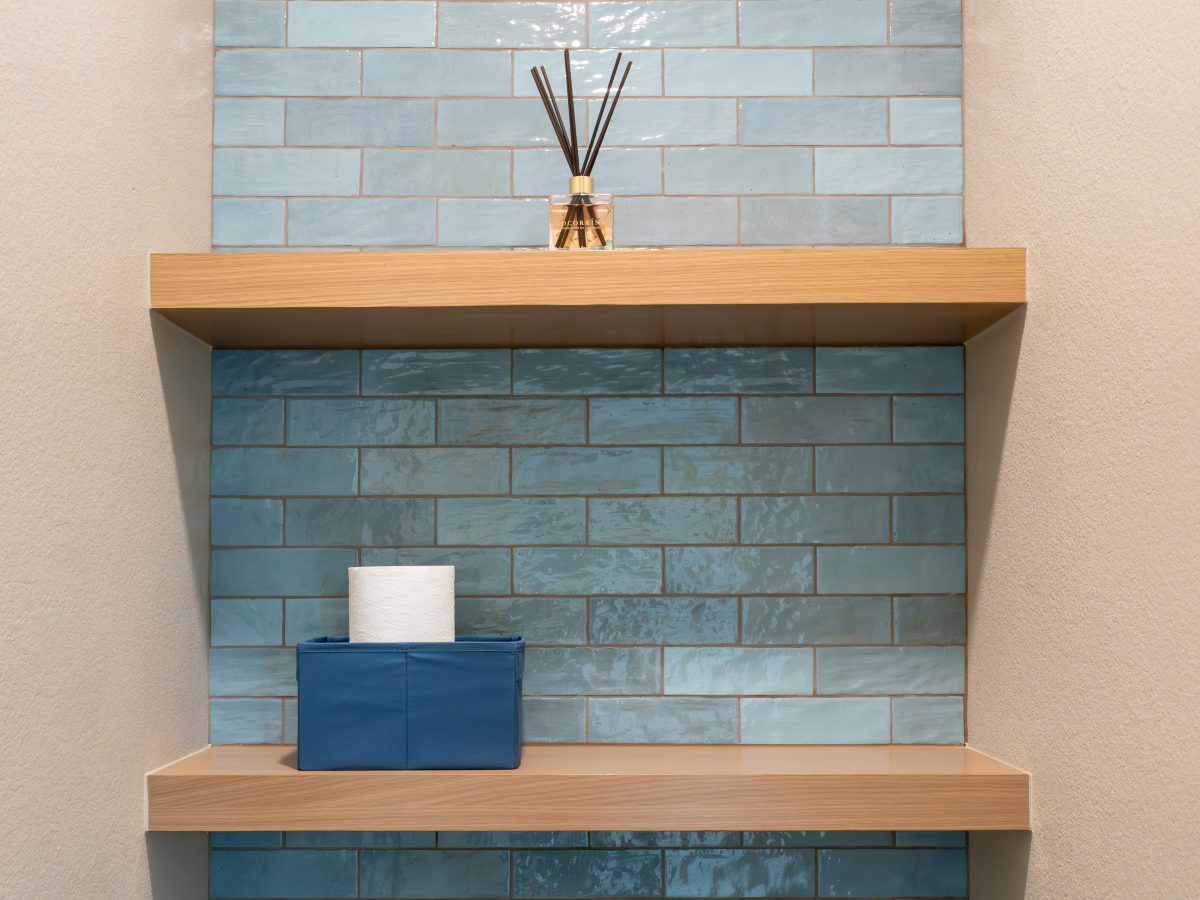 Toilet niche with handmade teal subway tile, warm oak floating shelves, and reed diffuser, Reveal Interior Design Las Vegas