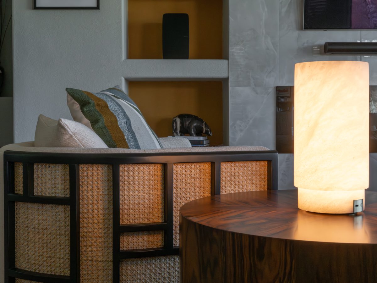 Living room with cane-back swivel chair, walnut side table, and glowing stone-look table lamp, Reveal Interior Design Las Vegas