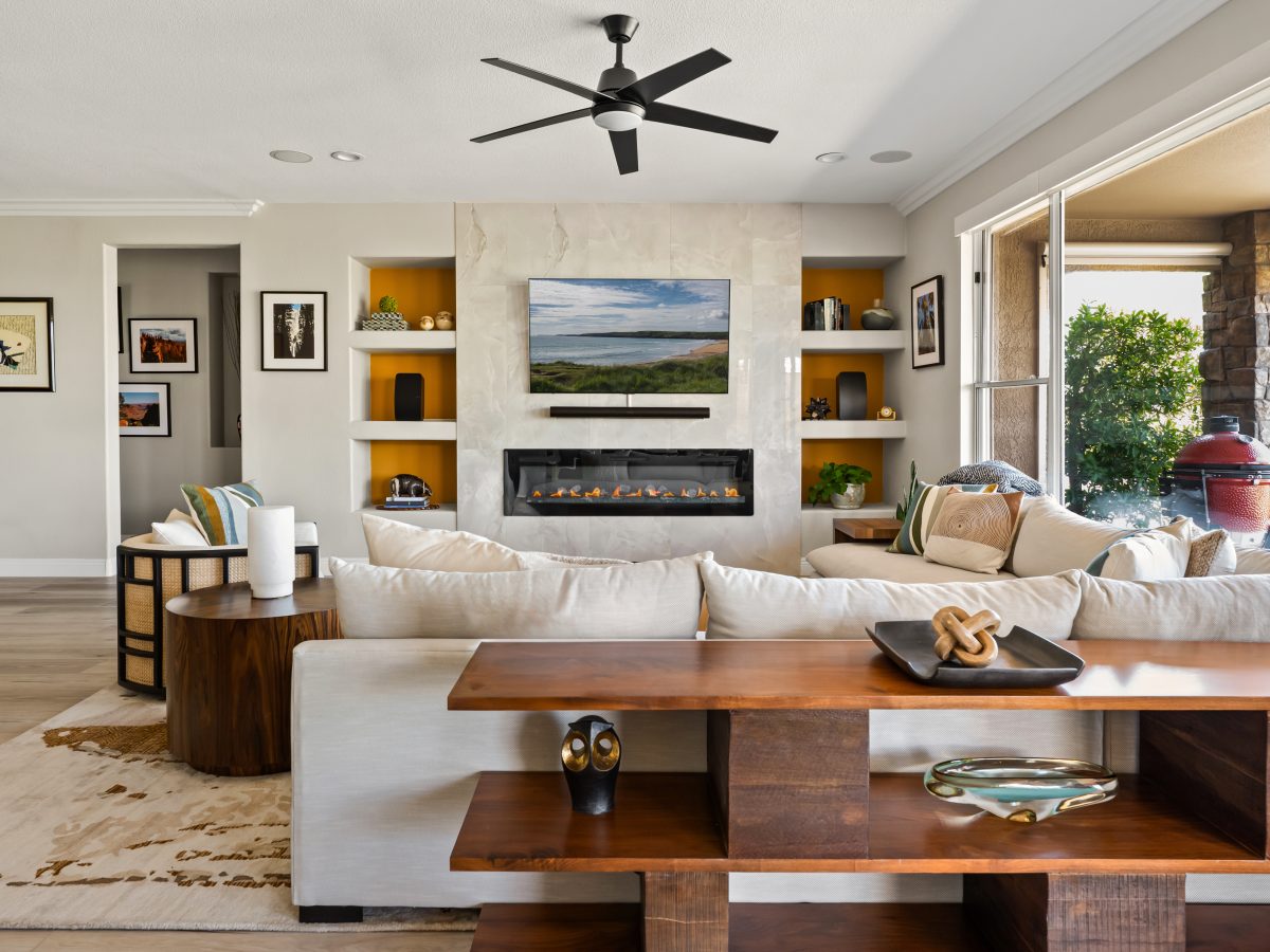 Living room with stone-surround fireplace, orange accent built-ins, and natural wood furnishings, Reveal Interior Design Las Vegas