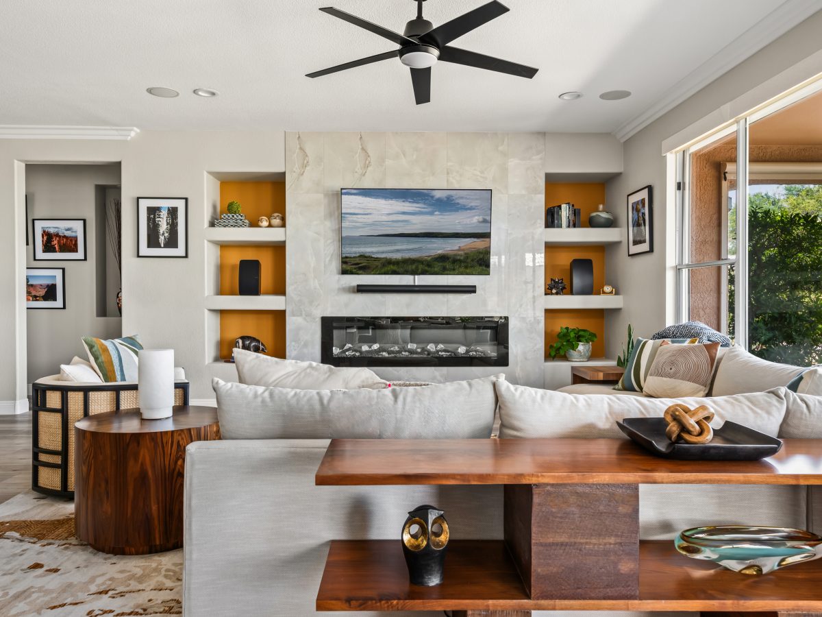 Living room with stone-clad media wall, orange accent built-ins, and walnut wood furnishings, Reveal Interior Design Las Vegas