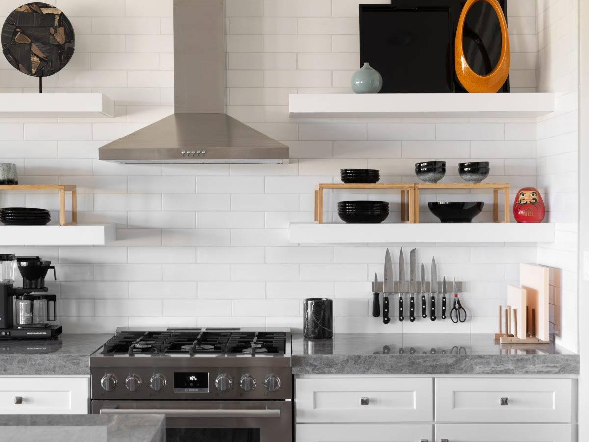 Modern white kitchen with open shelving, stainless range hood, and bold orange and black accent décor, Reveal Interior Design Las Vegas