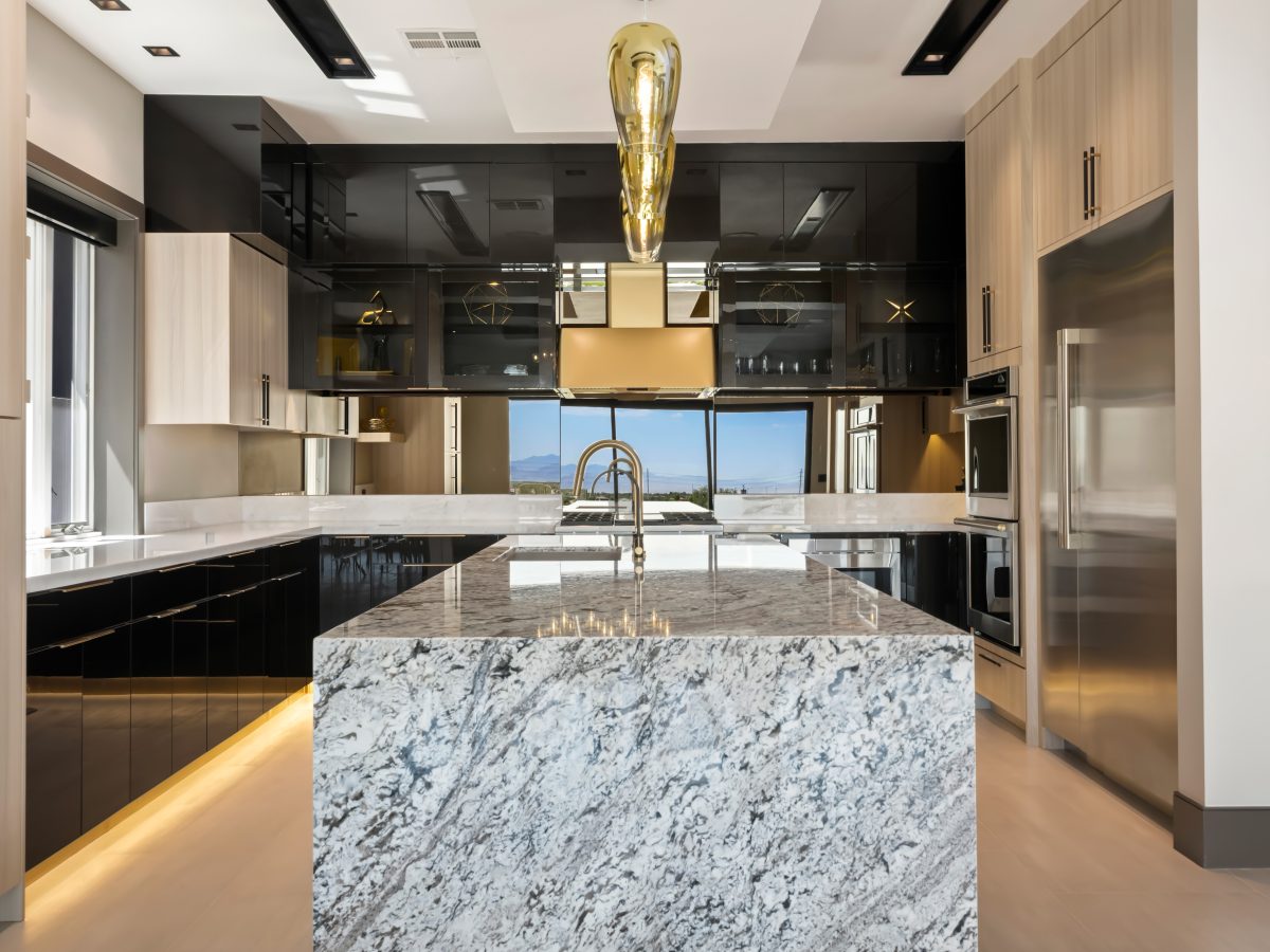 Luxury kitchen with granite waterfall island, charcoal gloss cabinetry, and gold accents, Reveal Interior Design Las Vegas