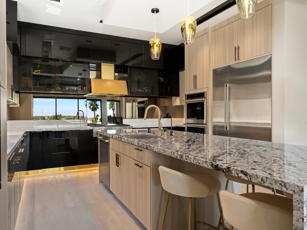Luxury kitchen with granite island, glossy charcoal cabinetry, and gold range hood, Reveal Interior Design Las Vegas