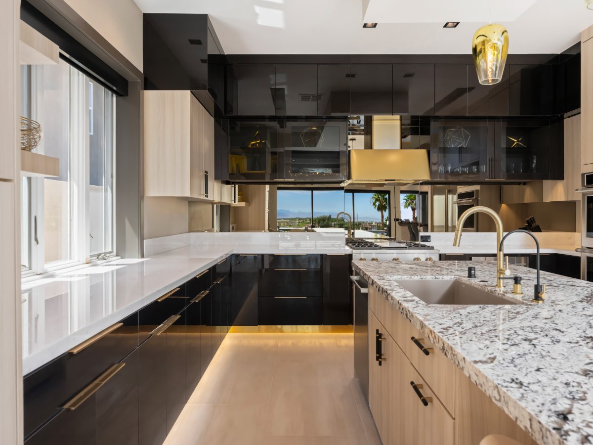 Luxury kitchen with granite island, glossy charcoal cabinetry, and gold fixtures, Reveal Interior Design Las Vegas