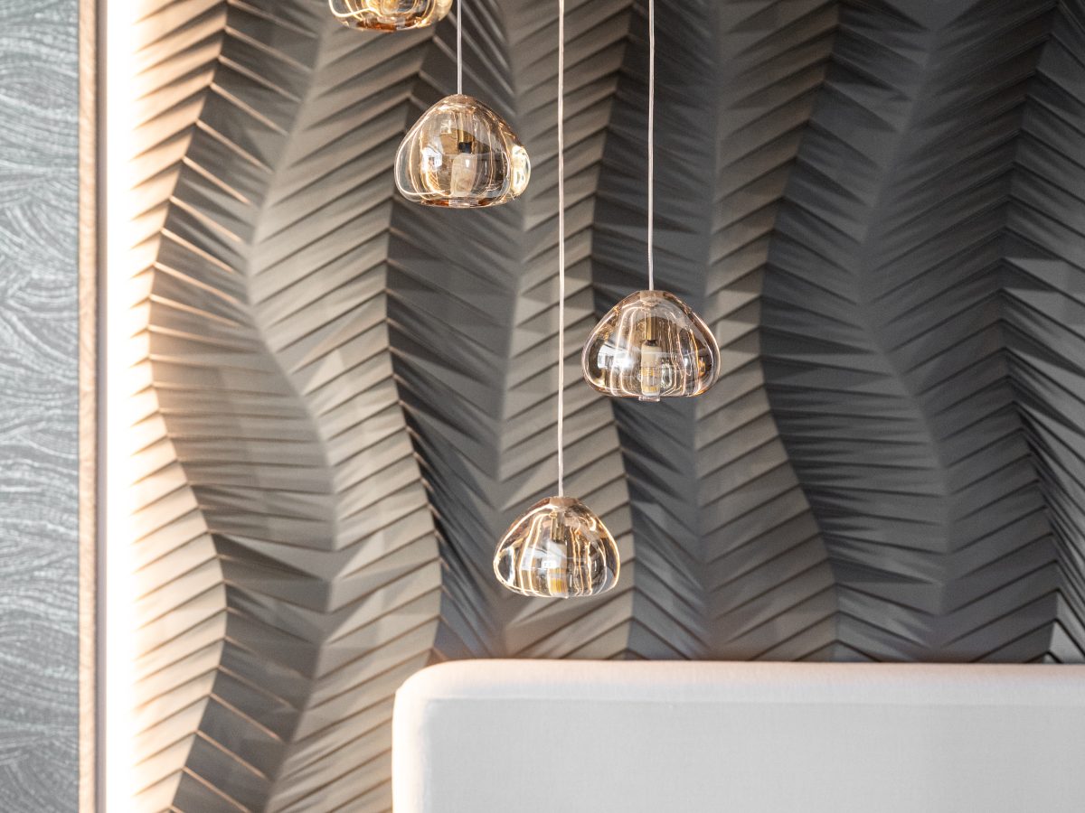 Primary bedroom with gold bronze textured wall panels, multi-drop pendants, and linear fireplace, Reveal Interior Design Las Vegas