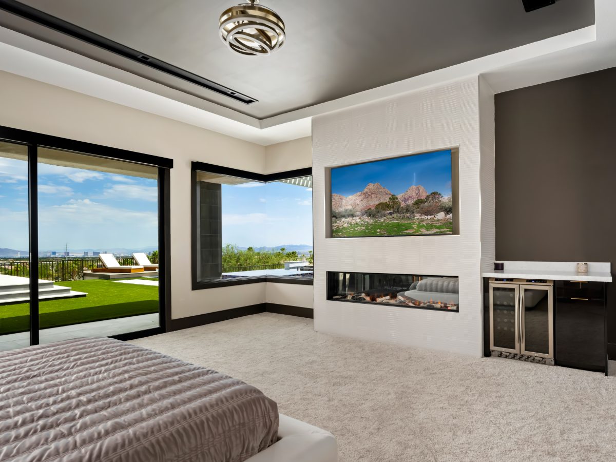 Primary bedroom with linear fireplace, recessed TV, corner glass walls and city views, Reveal Interior Design Las Vegas
