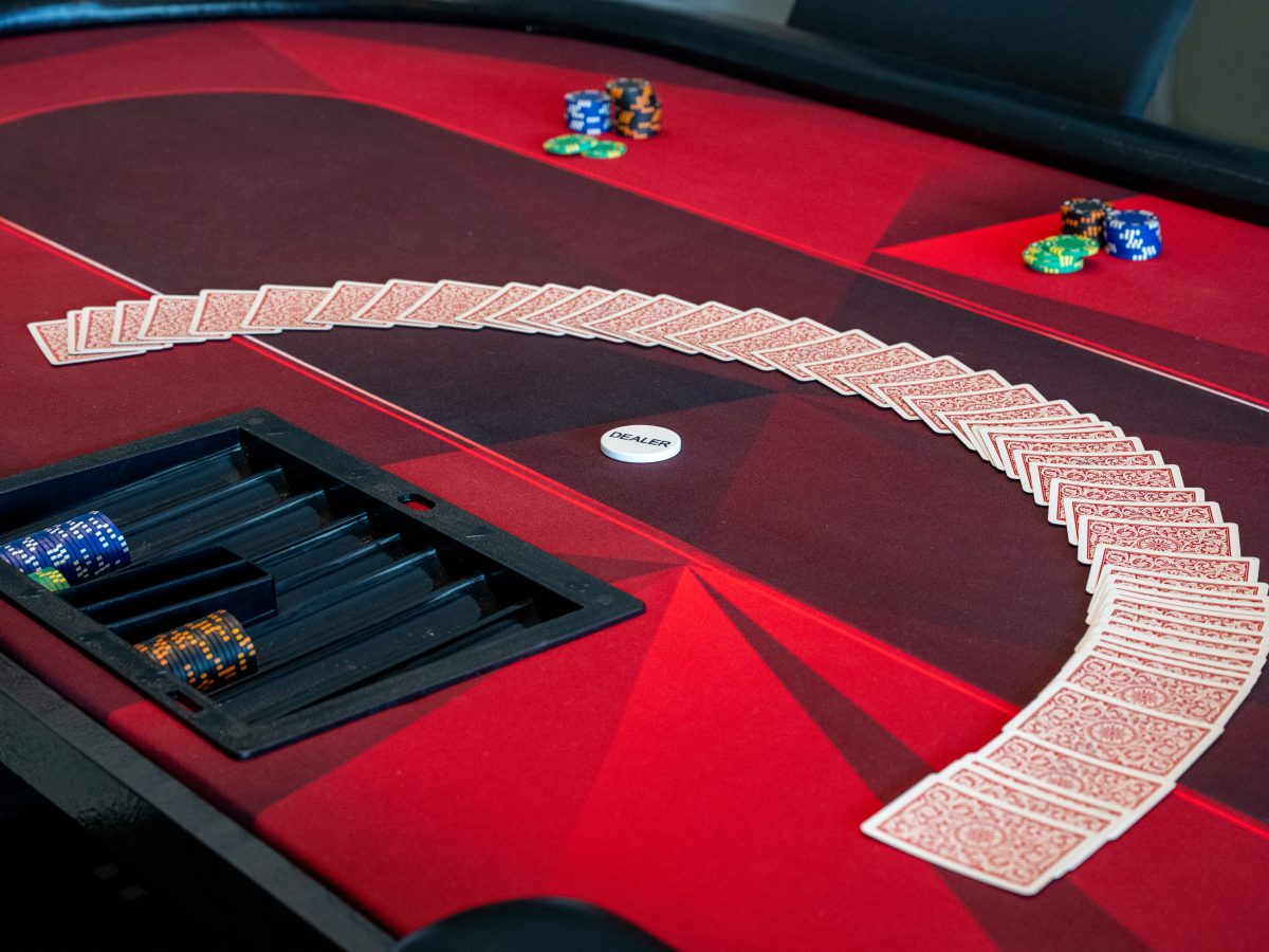 Game room crimson felt card table with dealer chip and spread deck, Reveal Interior Design Las Vegas
